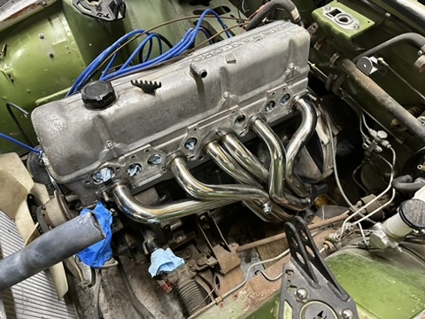 L-series engine with a shiny replacement tubular exhaust header fitted