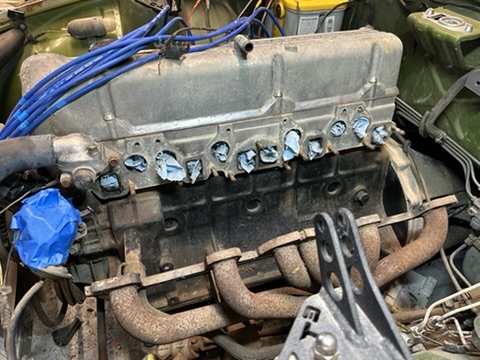 L-series engine with a weathered exhaust header and intake ports temporarily plugged