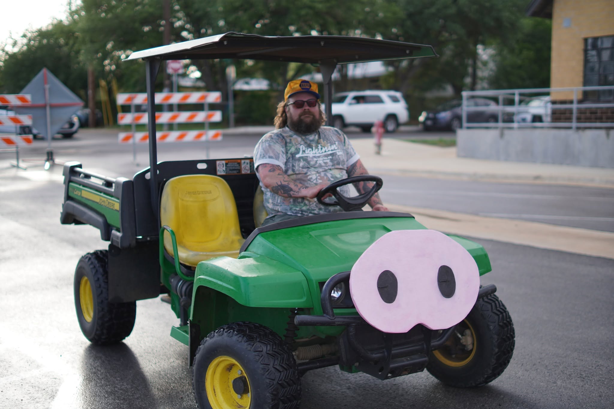 A driver in a green utility vehicle decorated with a pink pig snout